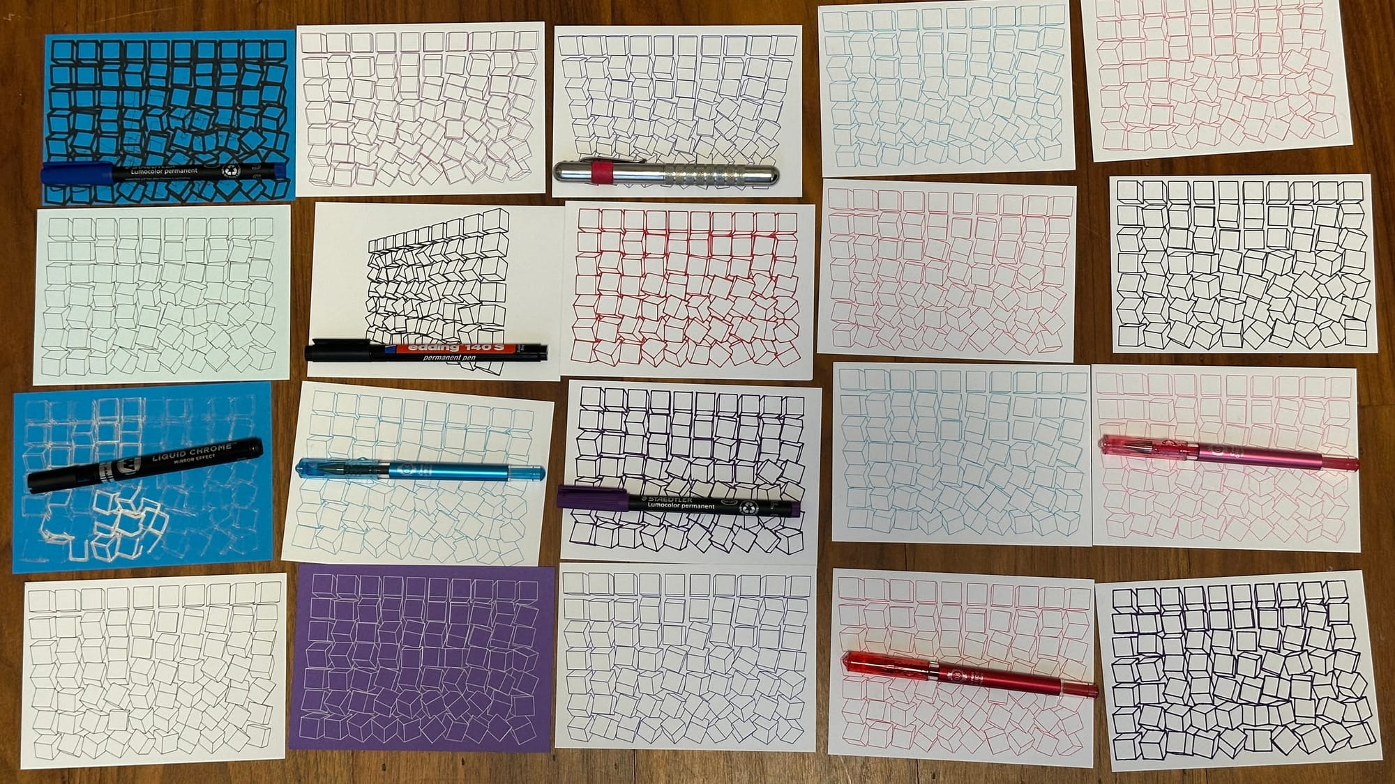 Twenty post cards arranged in a grid with their pens atop them