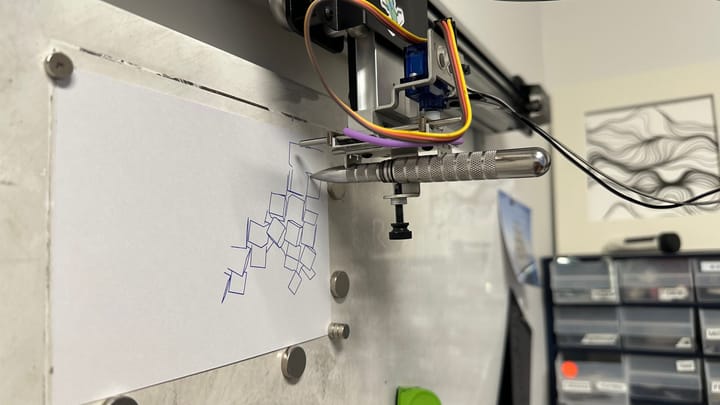 Plotter on a wall with a pen drawing boxes. Other art is in the background.